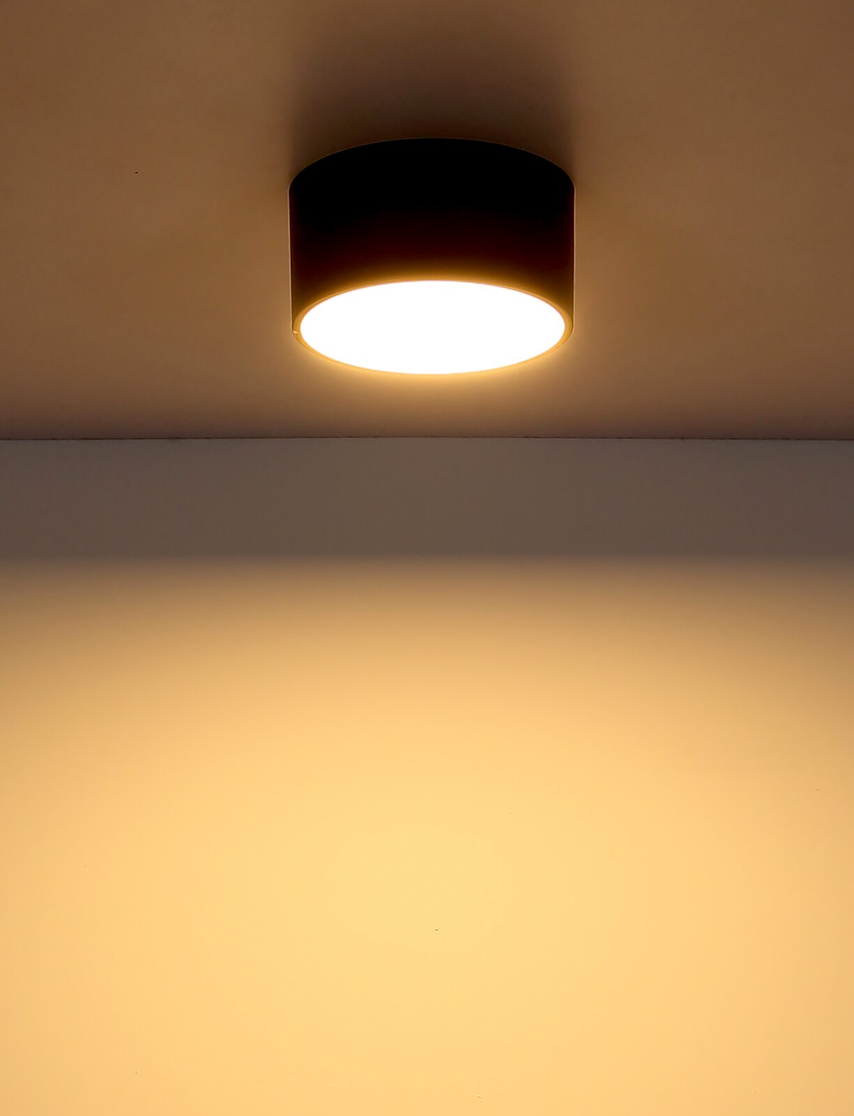 Moderne ronde plafondlamp in een zwarte behuizing, gezien van onderaf, met een warme lichtschijn op het plafond.