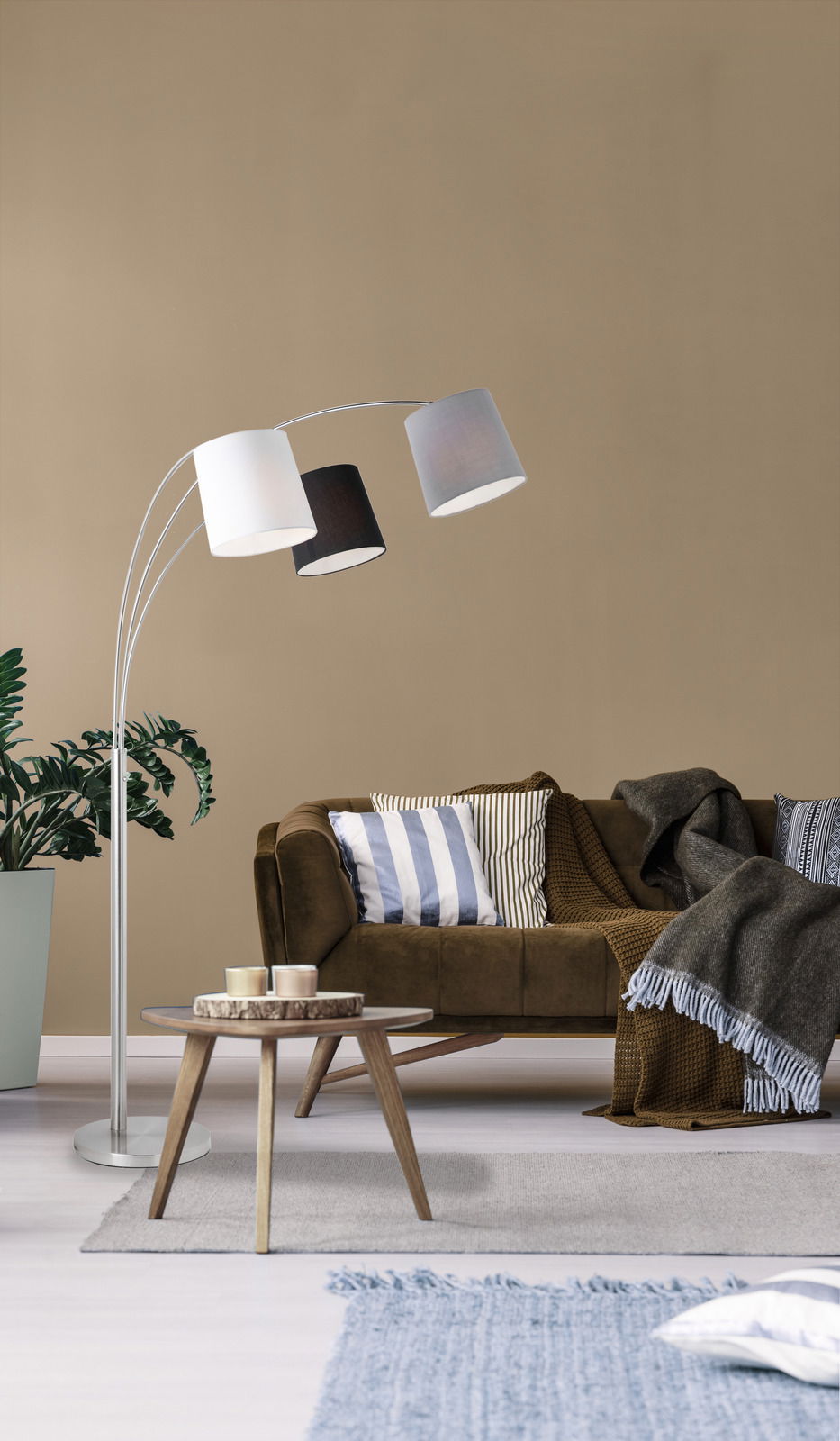 Moderne Stehleuchte aus Stahl mit drei unterschiedlich farbigen Lampenschirmen, seitliche Perspektive im Wohnzimmer.