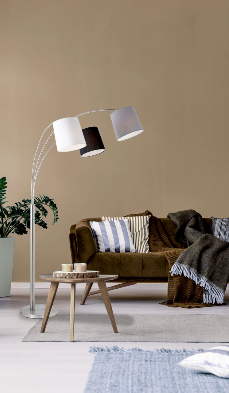 Moderne staande lamp van staal met drie lampenkappen in verschillende kleuren, zijaanzicht in de woonkamer.