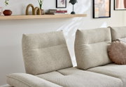 Close-up van een beige ligstoelcombinatie met twee gestoffeerde rugleuningen, versierd met een rond kussen; op de achtergrond een plank met decoraties.