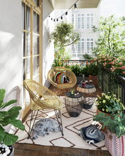 Gemütliche Balkonansicht mit zwei runden Beistelltischen aus Metall und Glas, umgeben von Rattan-Stühlen, Pflanzen und Dekorationen.