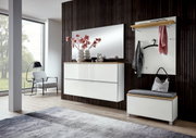 Vooraanzicht van een moderne garderobecombinatie in de hal: witte ladekast met houten plank en grote spiegel, daarnaast een wandgarderobe met plank, haken en zitbank tegen een donkere wand met houten lamellen.