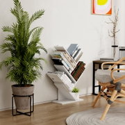 Weißes, modernes Bücherregal im Zickzack-Design mit mehreren Fächern, gefüllt mit Büchern, freistehend vor heller Wand im Wohnraum; Perspektive: frontale leichte Seitenansicht (3/4) auf das Regal.