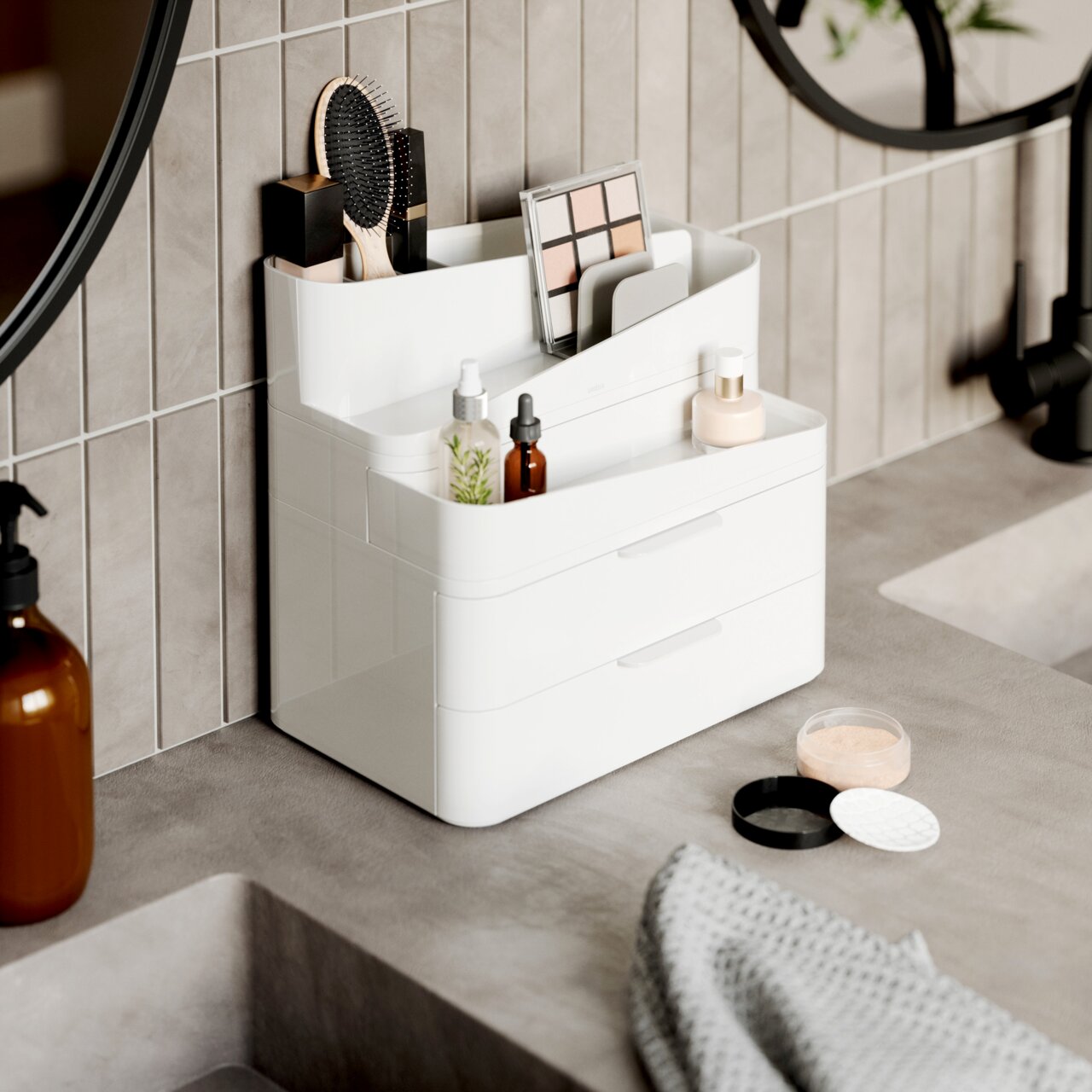 Weißer und grauer Glam Organizer mit mehreren Fächern und Schubladen, gefüllt mit Kosmetikartikeln, auf einer Badezimmerablage von der Seite betrachtet.