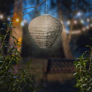 Hängende Solar Laterne in einem Garten bei Dämmerung, umgeben von Pflanzen, mit einem dekorativen Muster und warmem Licht.