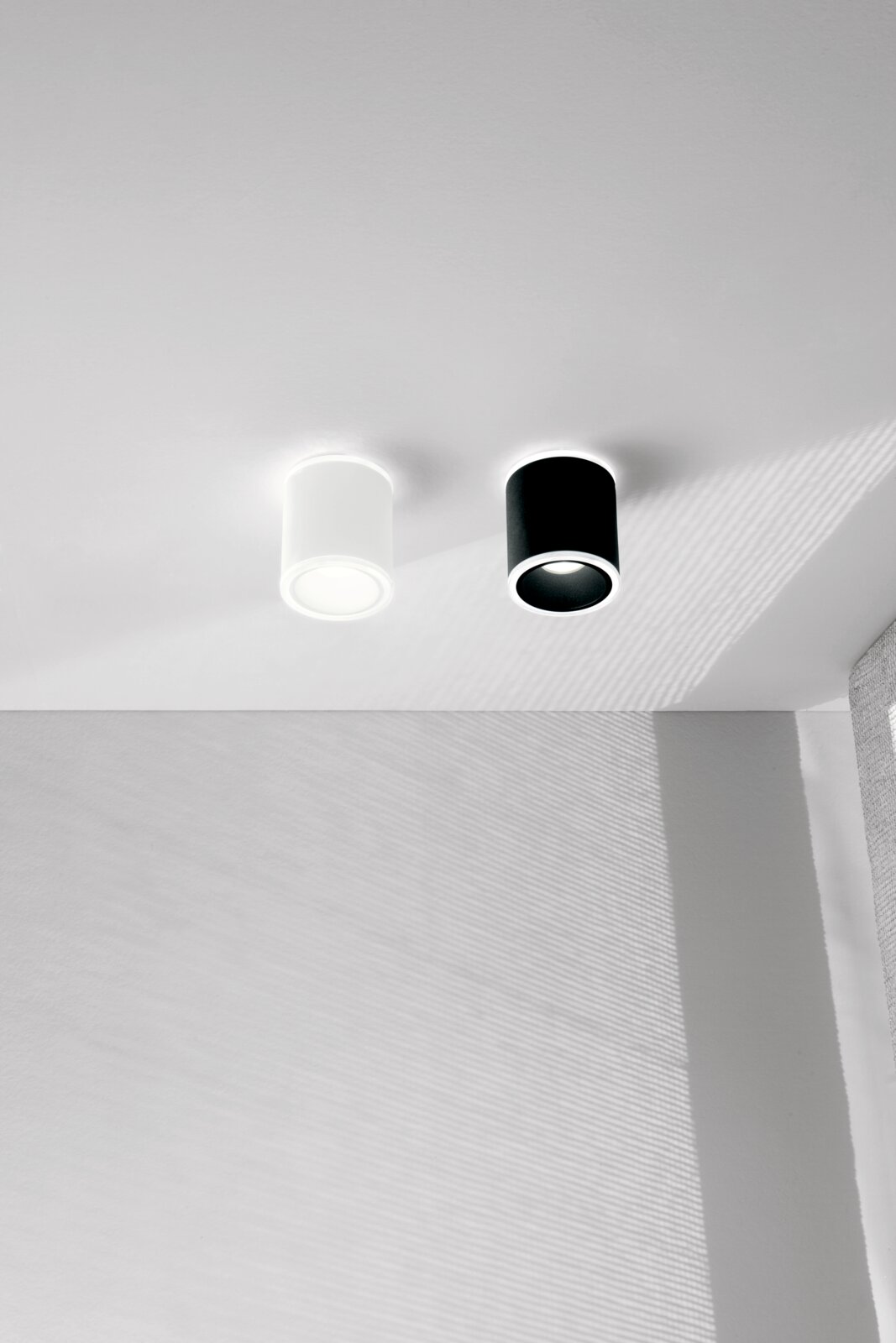 Twee cilindervormige LED-opbouwspots in zwart en wit, aan het plafond gemonteerd, gefotografeerd vanuit een zijaanzicht.