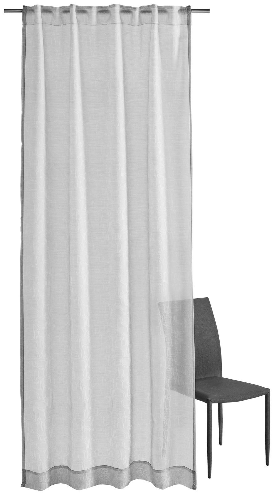 Grauer Vorhang mit Allover-Ornamentmuster, frontal fotografiert, neben einem Stuhl.