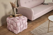 Rosa gepolsterter Hocker in Würfelform mit geflochtenem Design, von schräg oben fotografiert, neben einem Sofa und einem Tisch platziert.