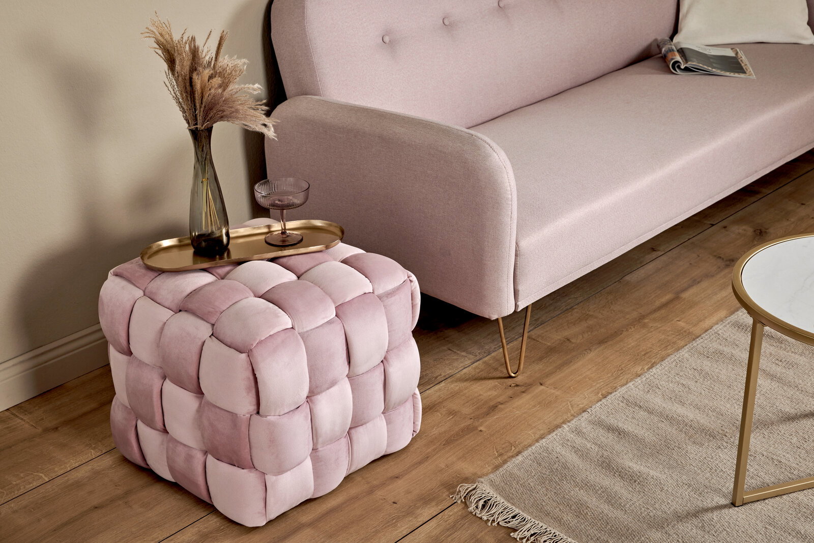 Jahnke Hocker WEB ART Rosa gepolsterter Hocker in Würfelform mit geflochtenem Design, von schräg oben fotografiert, neben einem Sofa und einem Tisch platziert.