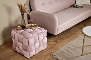 Rosa gepolsterter Hocker in Würfelform mit geflochtenem Design, von schräg oben fotografiert, neben einem Sofa und einem Tisch platziert.