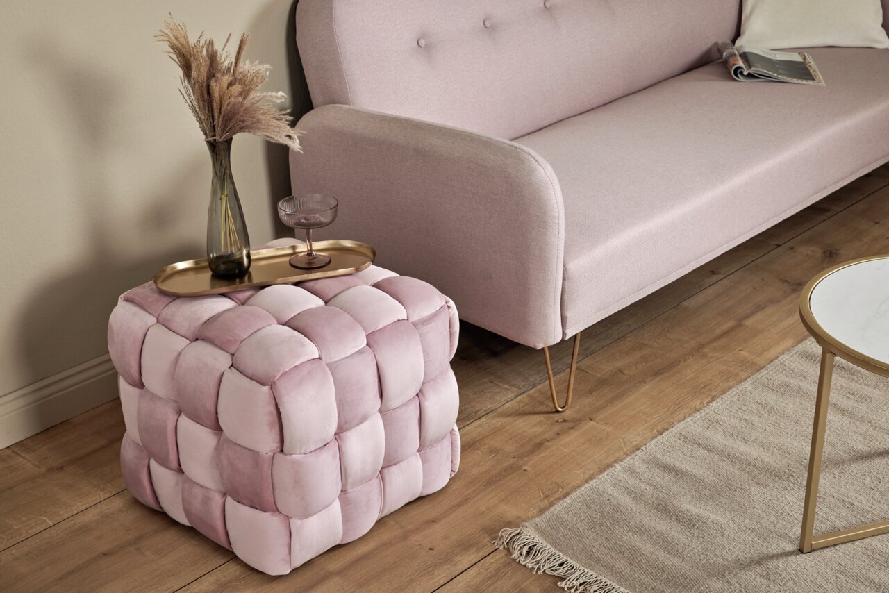 Jahnke Kruk WEB ART Roze, gestoffeerde kubusvormige poef met gevlochten patroon, gefotografeerd vanuit een schuine hoek van bovenaf, geplaatst naast een bank en een tafel.