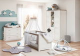 Helles Kinderzimmer mit einem stilvollen Kinderbett in Holzoptik, umgeben von einem Schrank, einer Kommode und Spielzeug, aus der Perspektive eines Betrachters, der den Raum betritt.