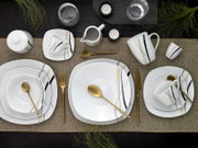 Draufsicht auf ein modern gedecktes Tischarrangement mit weißem Porzellan-Geschirrset (Teller, Schalen, Tassen, Kännchen) mit schwarzen, grauen und goldenen Linien sowie goldfarbenem Besteck auf Leinenläufer, ergänzt durch Gläser und Teelichter.