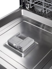 Close-up van de binnenkant van een roestvrijstalen vaatwasser met grijs doseerbakje voor vaatwasmiddel op de open deur, gefotografeerd vanuit een schuine bovenaanzichtperspectief.