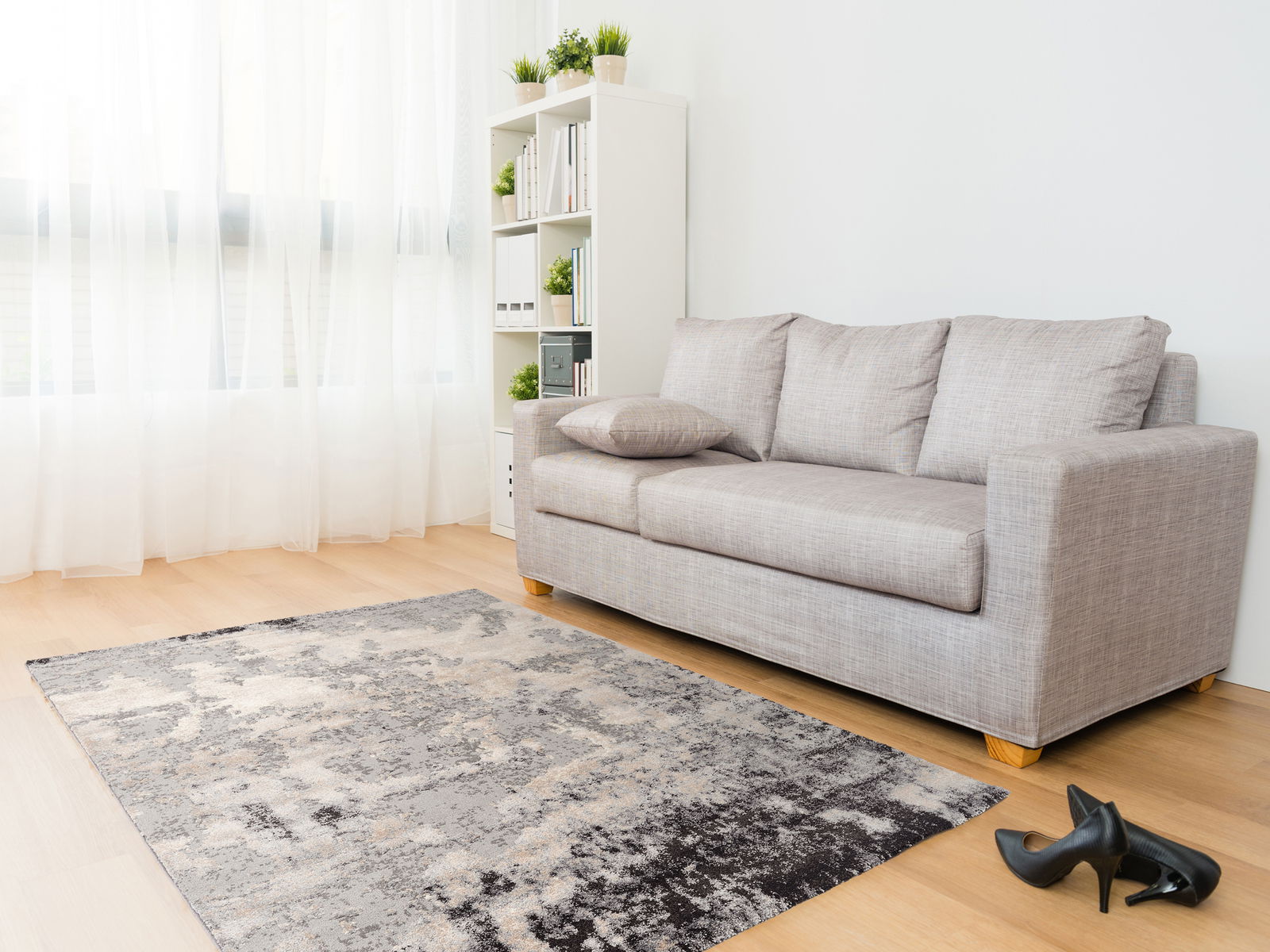 Moderner Designer Teppich in einem hellen Wohnzimmer mit grauem Sofa und Bücherregal, aus der Perspektive von schräg oben fotografiert.