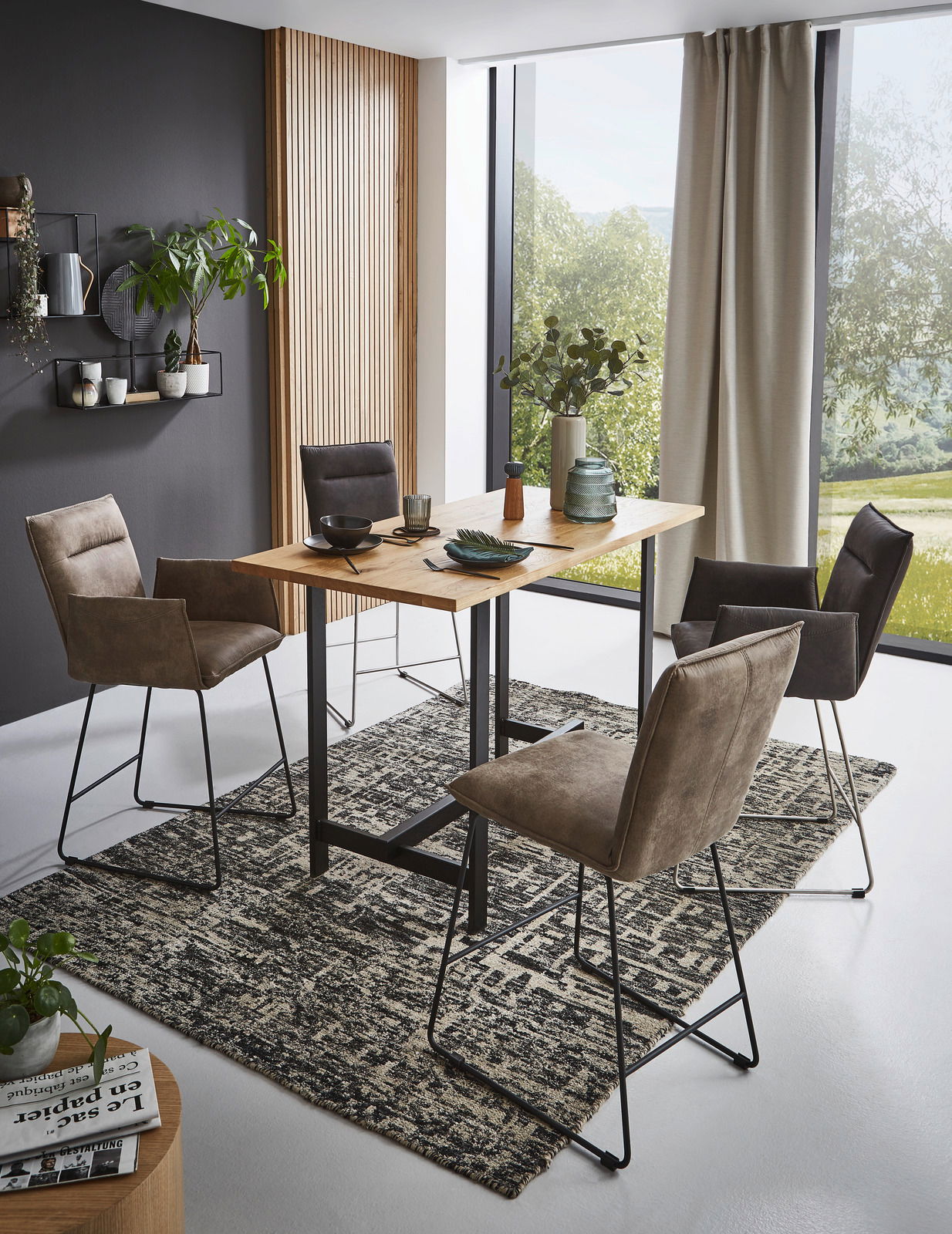 Moderne Esszimmer-Szene mit Valnatura Barsesseln und Tresentisch in einem hellen Raum mit großen Fenstern, seitliche Perspektive.