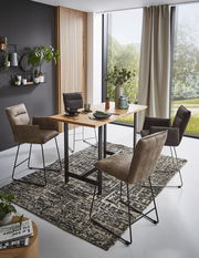 Moderne Esszimmer-Szene mit Valnatura Barsesseln und Tresentisch in einem hellen Raum mit großen Fenstern, seitliche Perspektive.