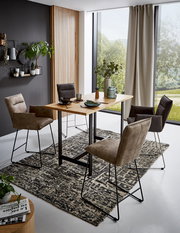 Moderne Esszimmer-Szene mit Valnatura Barsesseln und Tresentisch in einem hellen Raum mit großen Fenstern, seitliche Perspektive.