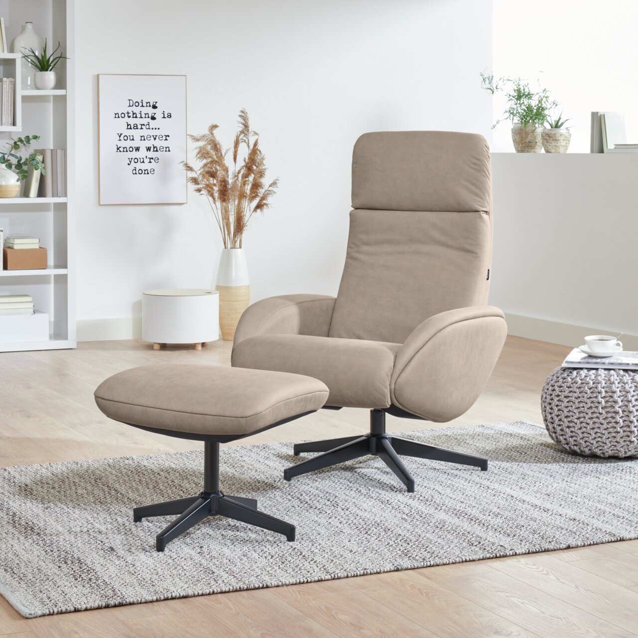 XORA Relaxfauteuil met voetenbankje MAYA Een beige relaxfauteuil met bijpassend voetenbankje op een tapijt in een moderne woonkamer, gezien vanuit de zijkant.