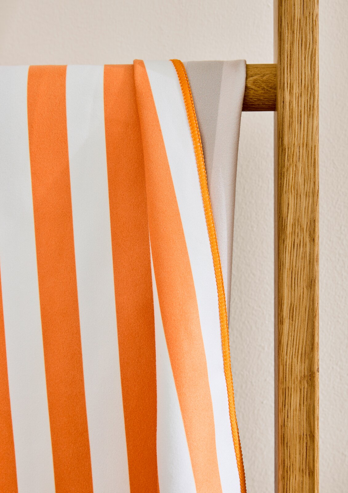 Nahaufnahme eines gestreiften Sporttuchs in Orange und Weiß, das über eine Holzleiter gehängt ist.