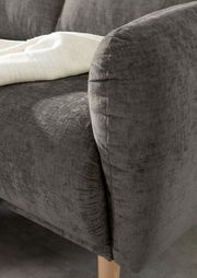 Nahaufnahme einer grauen Sofaecke mit abgerundeter Armlehne und Holzfuß, von der Seite betrachtet.
