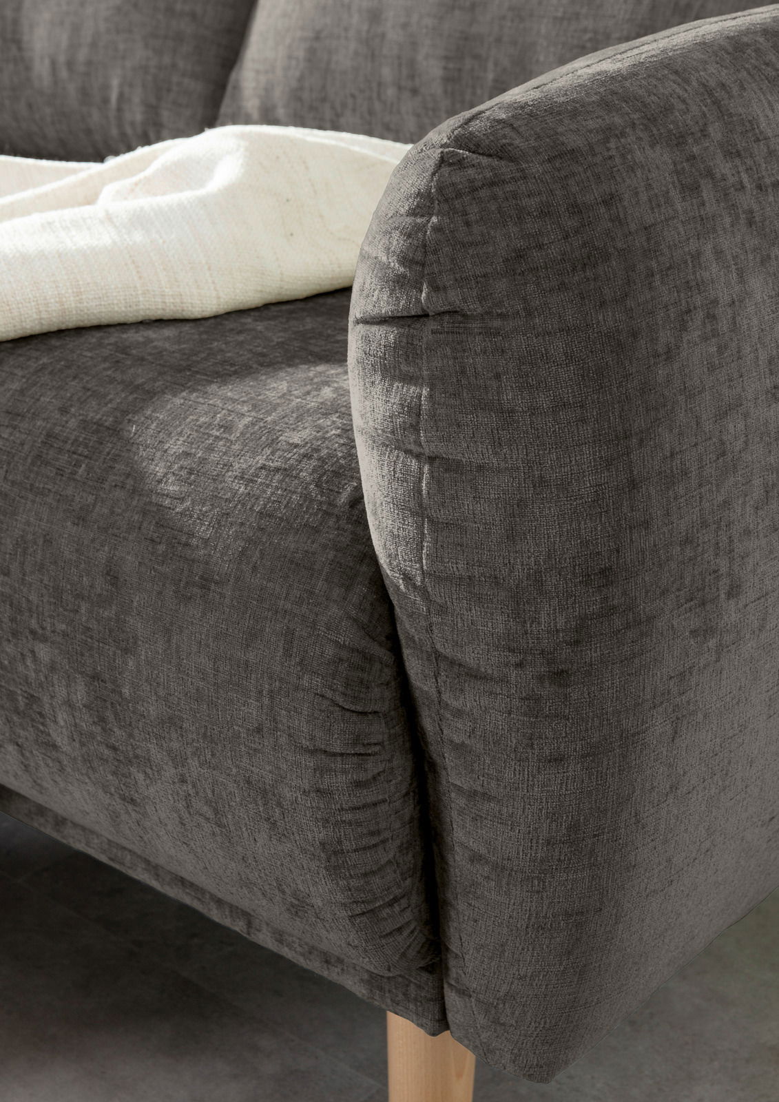 Nahaufnahme einer grauen Sofaecke mit abgerundeter Armlehne und Holzfuß, von der Seite betrachtet.