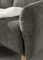 Nahaufnahme einer grauen Sofaecke mit abgerundeter Armlehne und Holzfuß, von der Seite betrachtet.