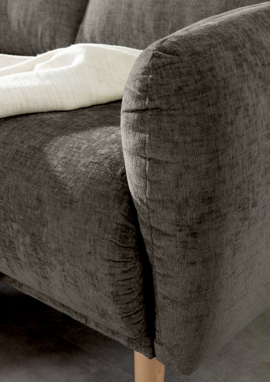 Nahaufnahme einer grauen Sofaecke mit abgerundeter Armlehne und Holzfuß, von der Seite betrachtet.