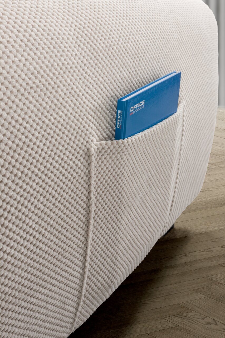 Nahaufnahme einer strukturierten, cremefarbenen Sofaecke mit einer Tasche, die ein blaues Notizbuch enthält, auf einem Holzboden.