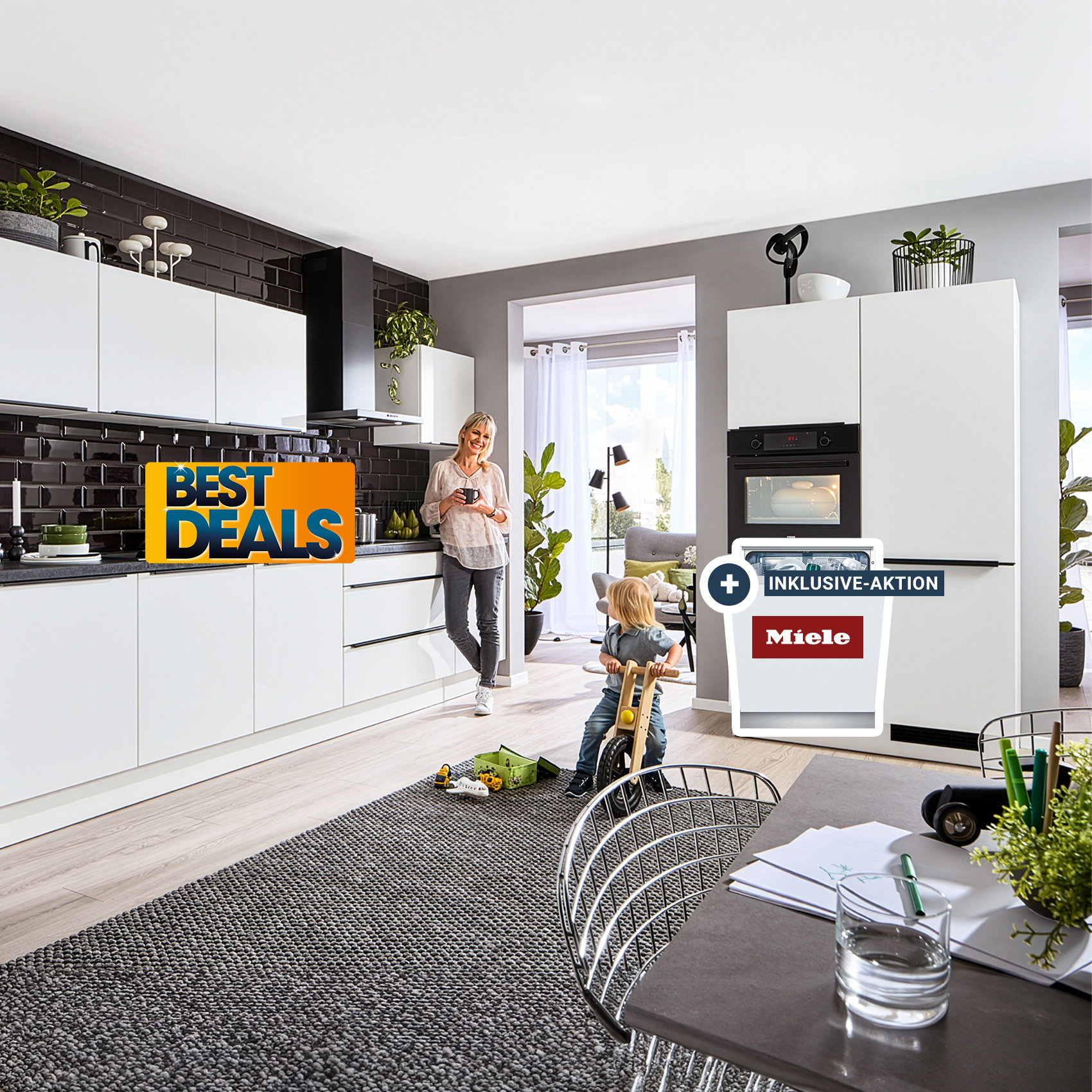 Moderne Küche mit weißen Schränken und dunkler Rückwand, Frau steht an der Arbeitsfläche, Kind spielt auf dem Boden