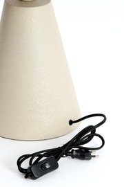 Close-up van een tafellamp met een conische kap en een zwarte kabel met schakelaar.
