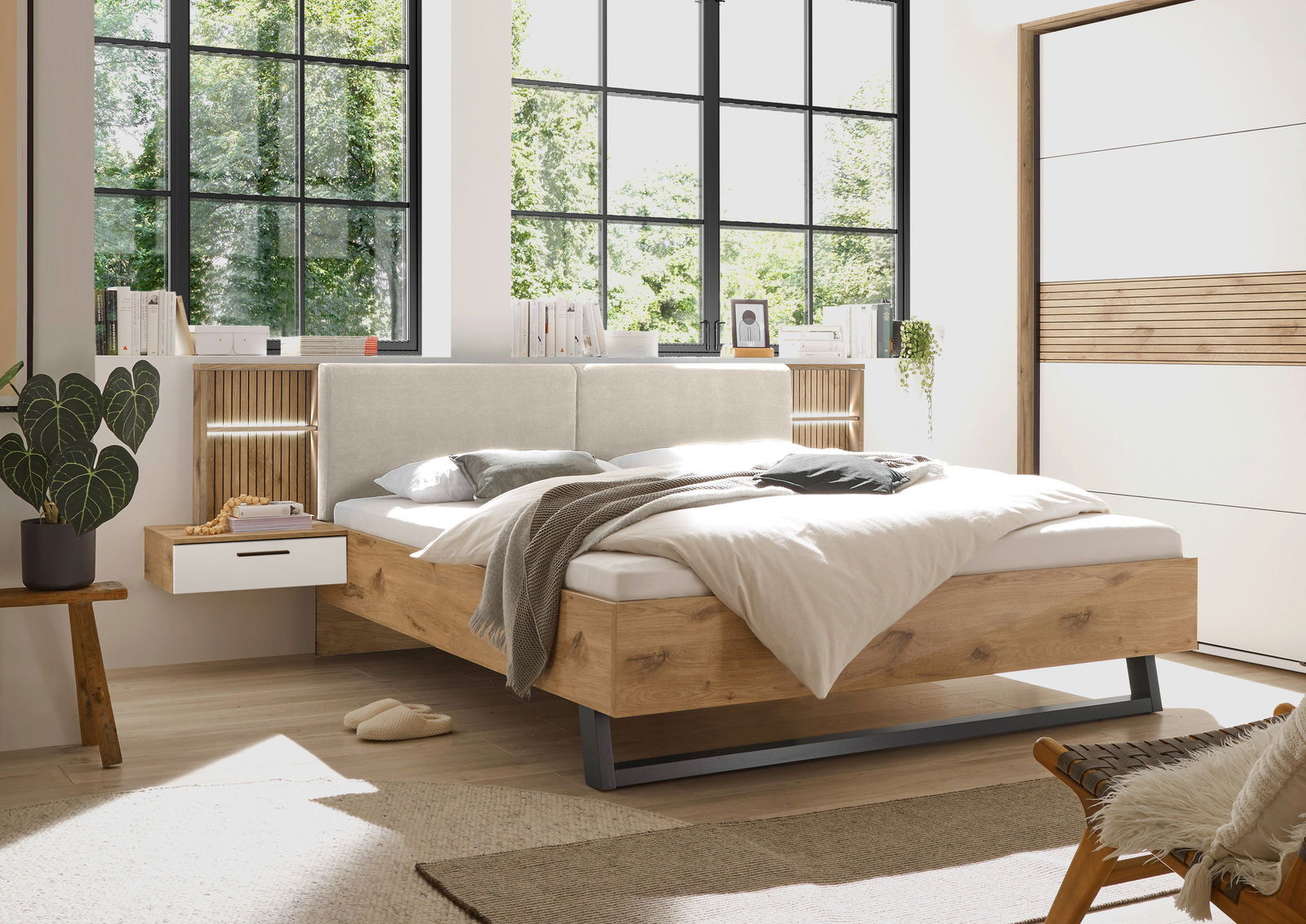 Modernes Schlafzimmer mit einem stilvollen Bett aus Holz und gepolstertem Kopfteil, seitlicher Perspektive. Das Bett ist von natürlichem Licht durch große Fenster umgeben, mit einem Nachttisch und dekorativen Elementen.