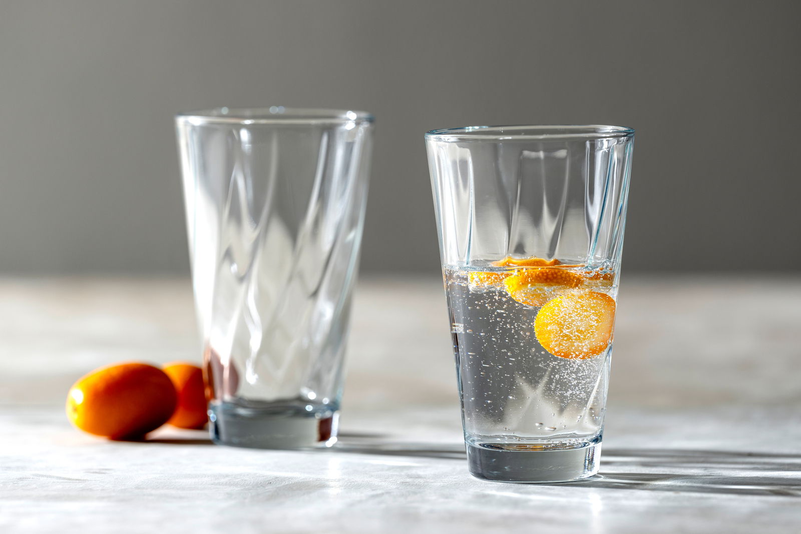 Leonardo Trinkglas TWIST Zwei Trinkgläser Twist von Leonardo, eines gefüllt mit sprudelndem Wasser und Orangenscheiben, auf einem Tisch mit seitlicher Perspektive.