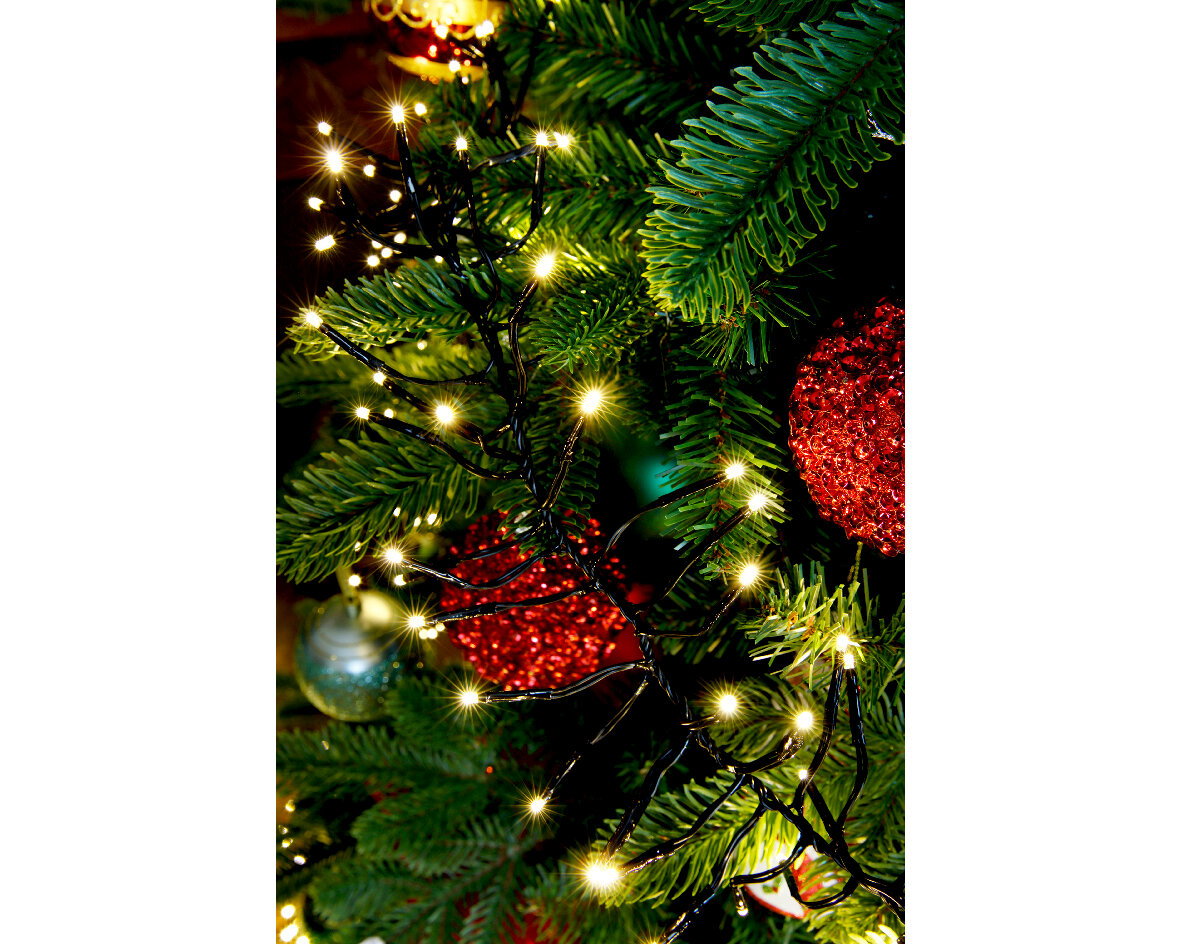 LED Clusterbeleuchtung in Nahaufnahme, umgeben von grünen Tannenzweigen und roten Weihnachtskugeln.