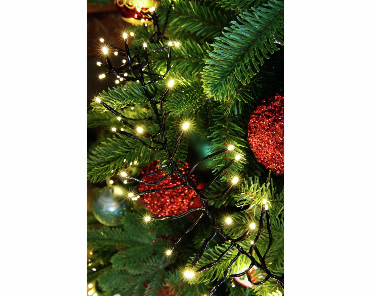 LED Clusterbeleuchtung in Nahaufnahme, umgeben von grünen Tannenzweigen und roten Weihnachtskugeln.