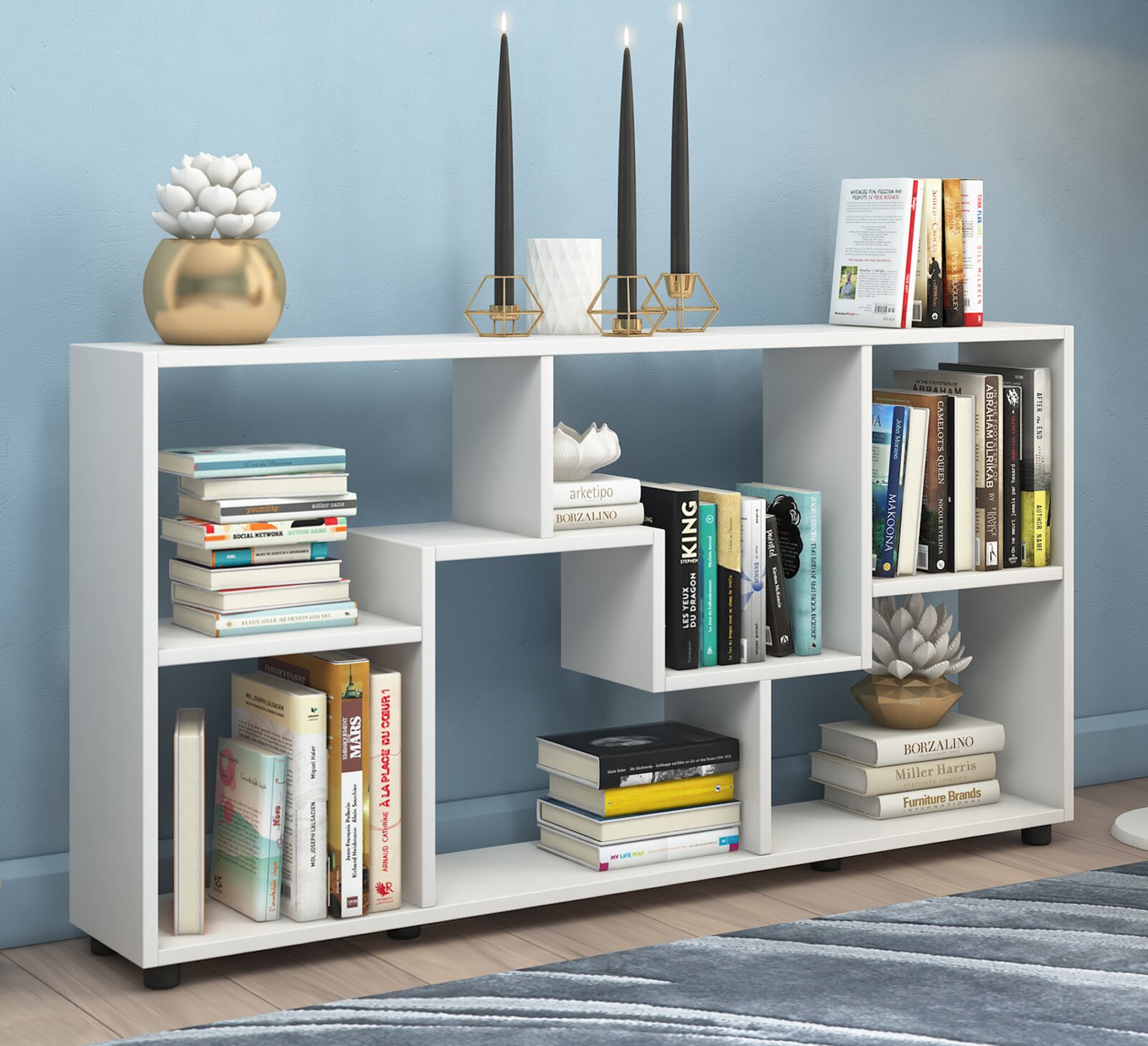 Modernes weißes Bücherregal mit asymmetrischen Fächern, dekoriert mit Büchern, Kerzenhaltern und Pflanzen, frontal aus leichter Seitenperspektive aufgenommen.