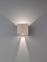 Moderne, quadratische LED-Wandleuchte in Weiß mit Up-&-Downlight, frontal an der Wand montiert und nach vorn fotografiert, erzeugt symmetrische Lichtkegel nach oben und unten auf grauer Wand