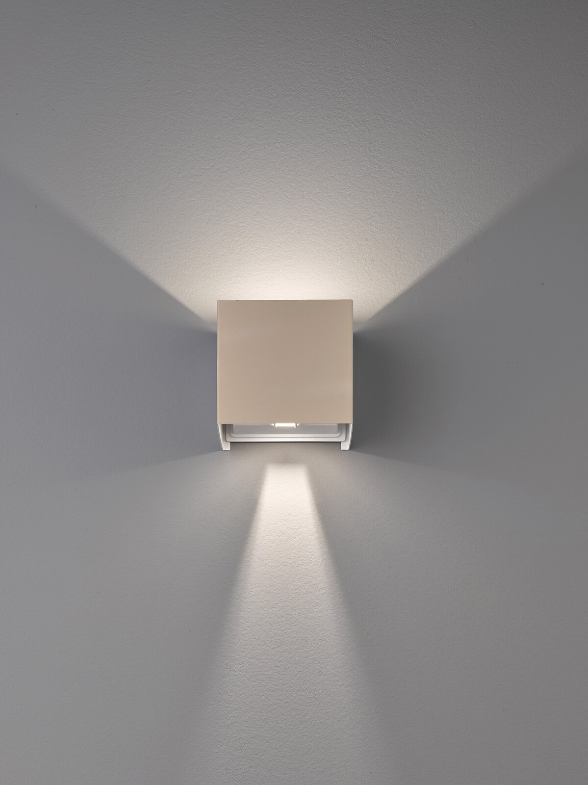 Moderne, quadratische LED-Wandleuchte in Weiß mit Up-&-Downlight, frontal an der Wand montiert und nach vorn fotografiert, erzeugt symmetrische Lichtkegel nach oben und unten auf grauer Wand