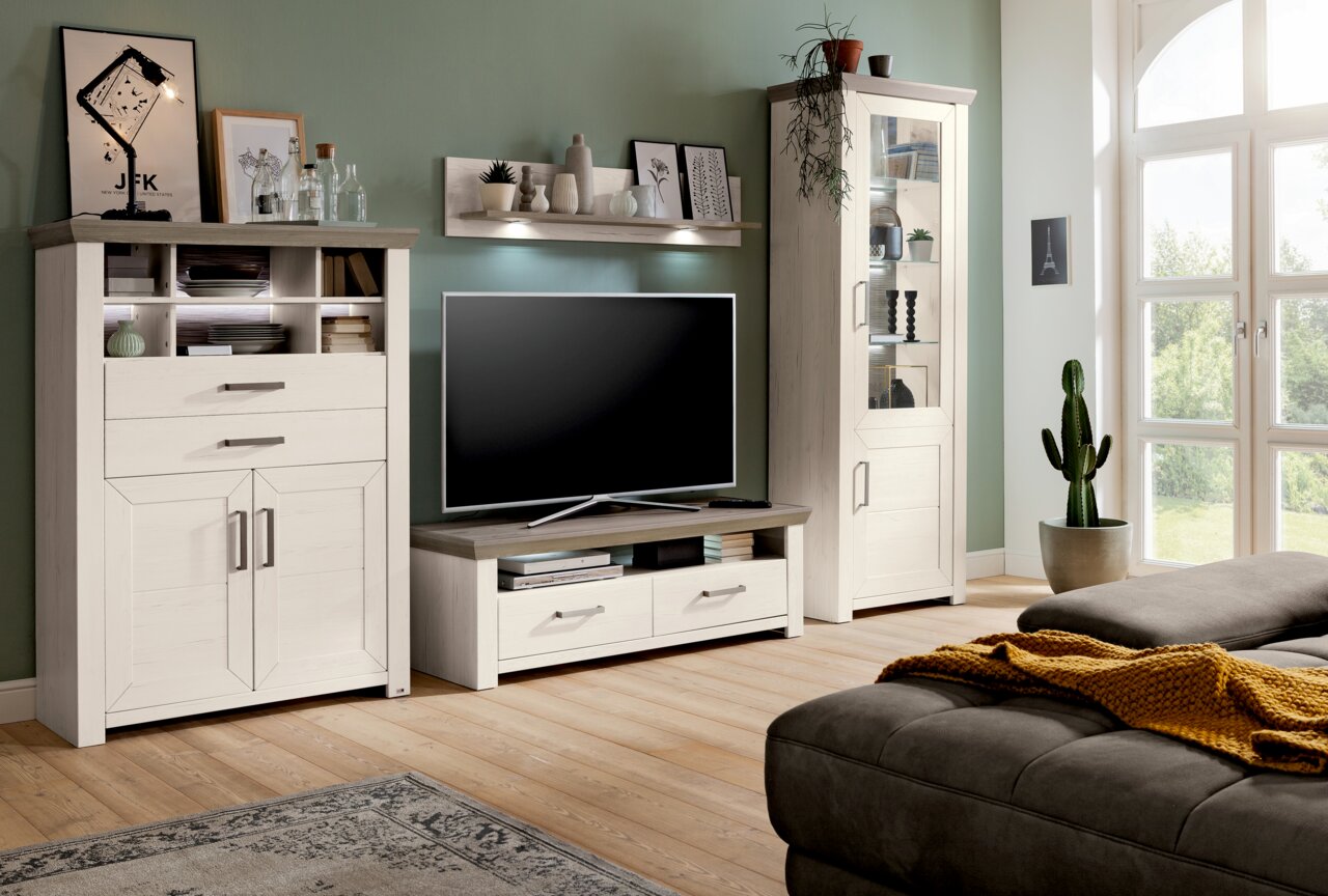 Wohnzimmermöbel-Set in heller Holzoptik mit Highboard, Lowboard und Vitrine, dekoriert mit Pflanzen und Bildern, seitliche Perspektive.