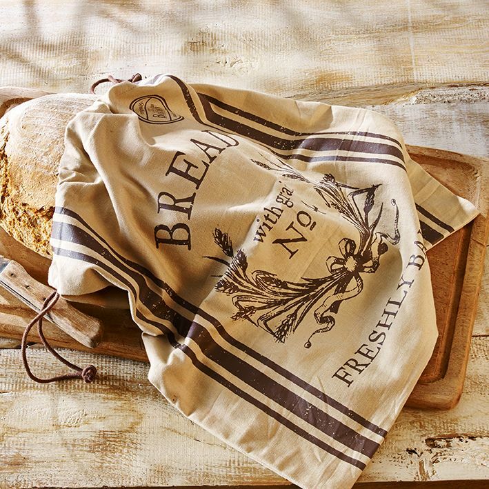 Birkmann Brotbeutel FRESHLY BAKED Brotbeutel mit der Aufschrift 'Freshly Baked' und dekorativem Design, auf einem Holztisch liegend, teilweise ein Laib Brot sichtbar. Perspektive von oben.