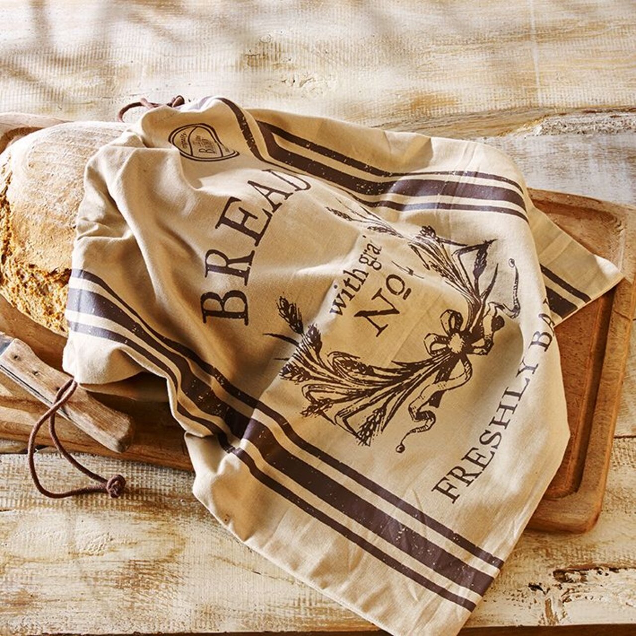 Birkmann Broodzak FRESHLY BAKED Een broodzak met het opschrift 'Freshly Baked' en een decoratief ontwerp, liggend op een houten tafel, waarbij een deel van een brood zichtbaar is. Aanzicht van bovenaf.