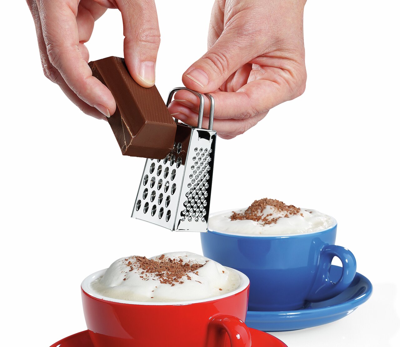 Mini-Vierkantreibe in der Hand, die Schokolade über einer Tasse mit Milchschaum reibt, seitliche Perspektive.