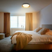 Ronde plafondlamp met warm wit licht en goudkleurige binnenring, van schuin onderen gezien in een sfeervolle slaapkamer