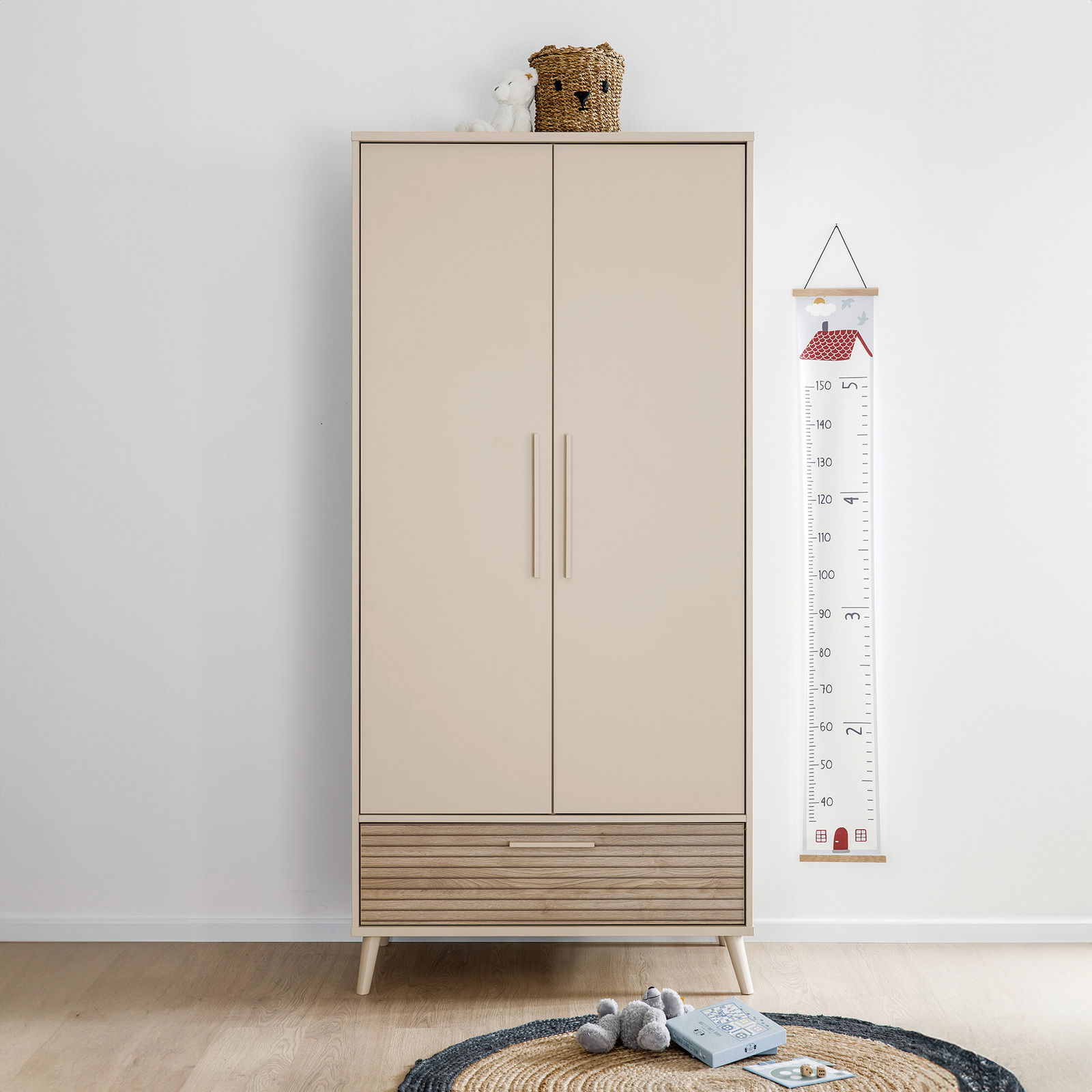 Moderner Kleiderschrank mit zwei Türen und einer Schublade in hellem Holzdesign, frontal fotografiert. Dekoriert mit einem Korb und einem Stofftier auf der Oberseite.