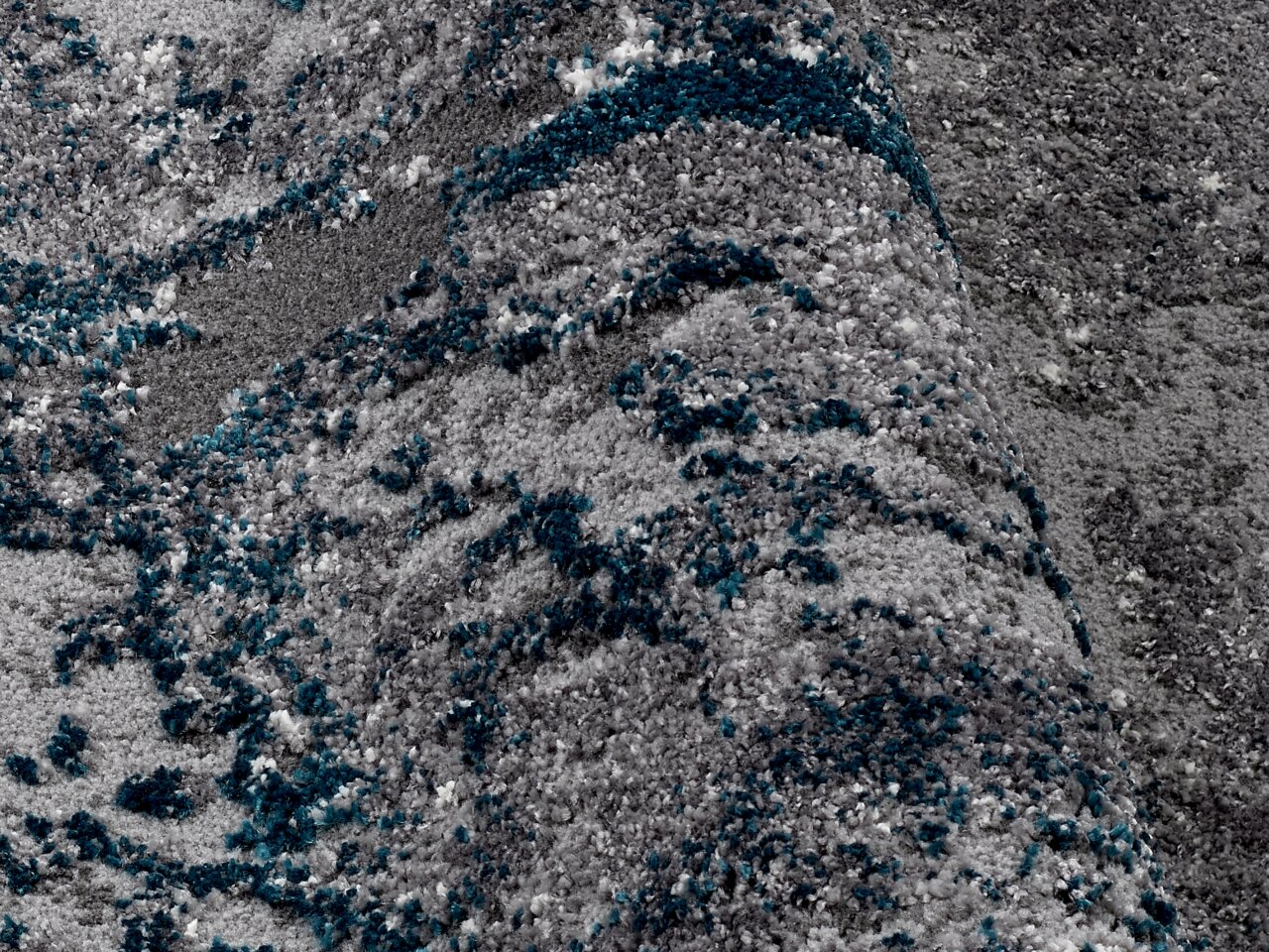 Nahaufnahme eines Designer Teppichs mit grauen und blauen Mustern, perspektivisch von oben fotografiert.