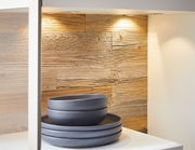 Nahaufnahme einer Vitrine mit Holzrückwand und Beleuchtung, die dunkelgraue Teller und Schalen präsentiert.