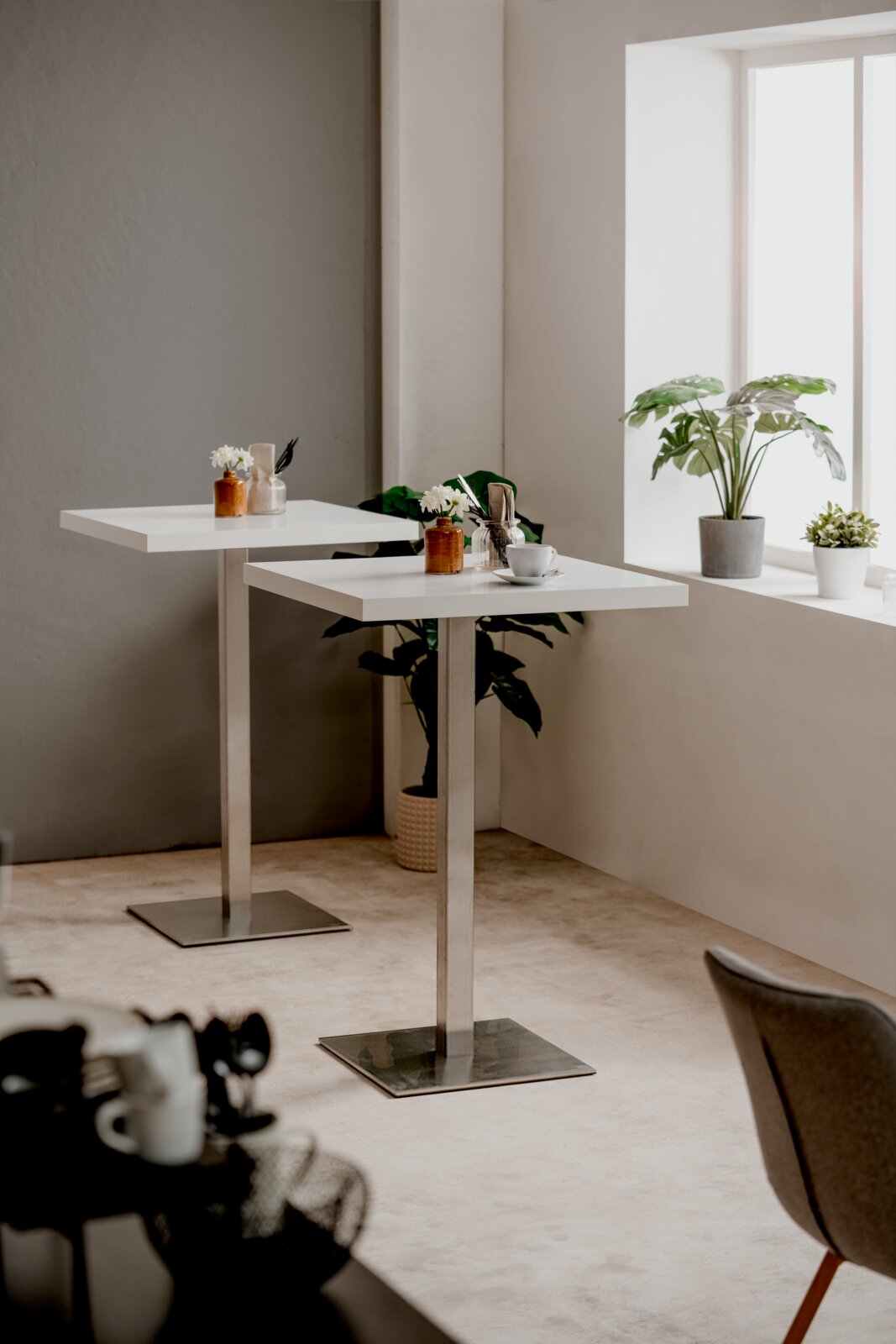 Moderner Bartisch QUADRATO mit weißer Tischplatte und Metallgestell, seitliche Perspektive, dekoriert mit Pflanzen und Geschirr.