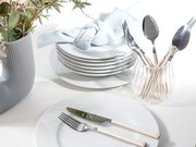 Elegantes Tafelservice mit gestapelten weißen Tellern, Besteck in einem Glas und einer blauen Serviette, aus der Vogelperspektive fotografiert.