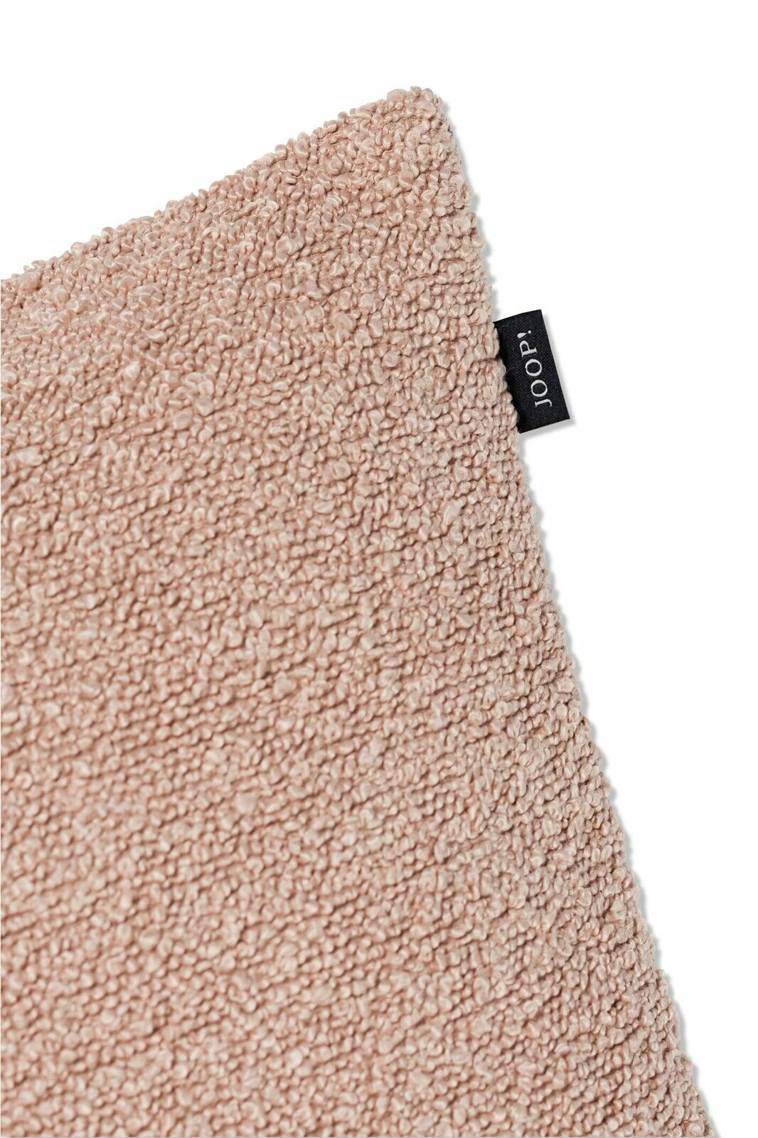 Nahaufnahme einer beigen Zierkissenhülle mit flauschiger Textur und einem kleinen schwarzen Etikett an der Seite.