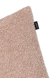 Nahaufnahme einer beigen Zierkissenhülle mit flauschiger Textur und einem kleinen schwarzen Etikett an der Seite.